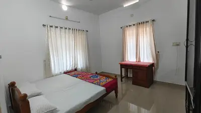 a bedroom with a bed and a table and windows at Havenza Homestayz in Athirappilly