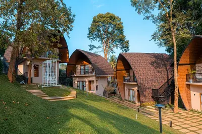 a group of three houses with trees and grass at Golf Valley Luxury Resort Wayanad in Vythiri
