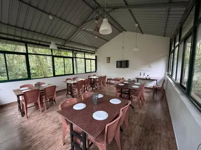 a dining room with tables and chairs and windows at Manuvan Estate Stay in Kushālnagar