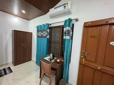 a room with a table and a desk with blue curtains at Manuvan Estate Stay in Kushālnagar