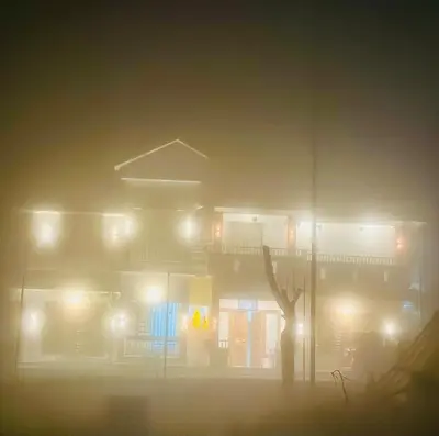 a building in the fog with a tree in the foreground at Zonooro Homestay Vythiri in Vythiri