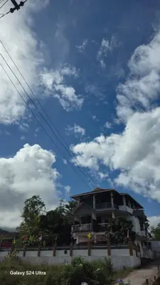 a building in front of a blue sky with clouds at Azhagumail Honey Resort Kanthalloor in Kanthalloor