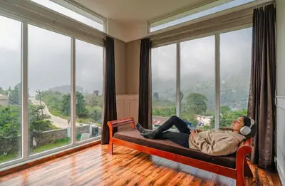 a woman laying on a couch in a room with large windows at EKOSTAY - Apollo Villa in Kodaikānāl