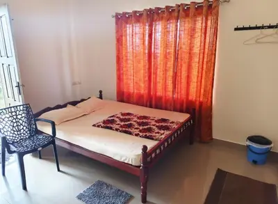 a bedroom with a bed and a chair and a window at Darshanam Inn in Guruvāyūr