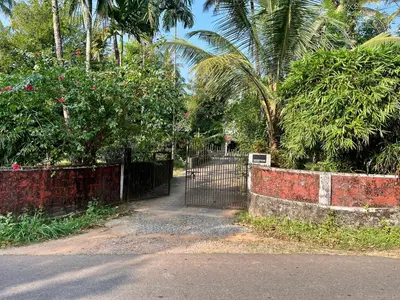 a gate in a garden with trees and palm trees at HARSHAM Eco Village in Puthuppādi