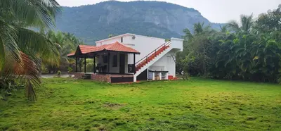 a small house in a field with a mountain in the background at LBS Farms in Coimbatore