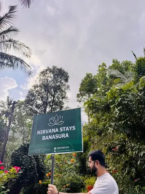 a man standing next to a sign in a garden at Nirvana Stays Banasura -Lotus in Wayanad