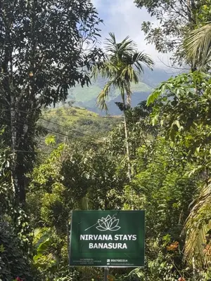 a sign in the middle of a forest with mountains in the background at Nirvana Stays Banasura -Lotus in Wayanad