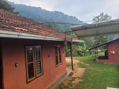 a red house with a mountain in the background at Dream Acres Mudhouse in Vallikavungal