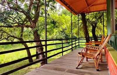 a porch with two chairs and a table and a fence at Jungle Hut Resort in Masinagudi