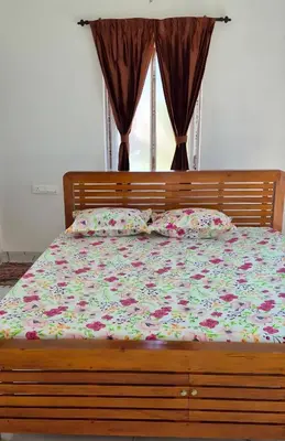 a bed with a floral comforter and pillows and a window at Stay41 in Vālpārai