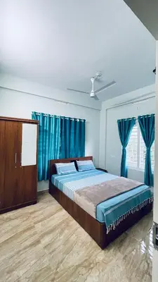 a bedroom with a large bed with blue curtains at The Karlyle Homestay in Sultan Bathery