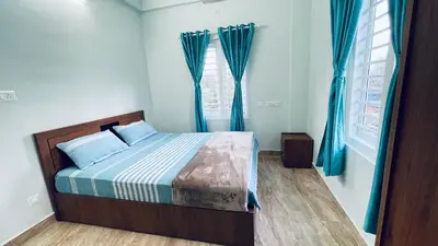 a bedroom with a bed with blue curtains at The Karlyle Homestay in Sultan Bathery