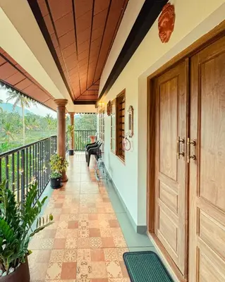 a porch with a wooden door and a balcony at Pochans Zen in Thattakād