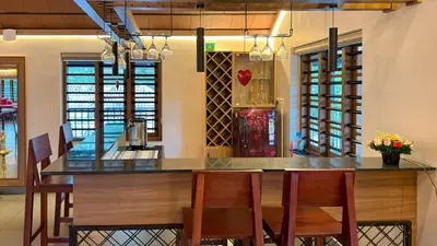 a kitchen with a bar with chairs and a table at Pochans Zen in Thattakād