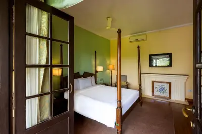 a bedroom with a white bed and a fireplace at amã Stays & Trails - Cottabetta Bungalow, Coorg in Gonikoppal