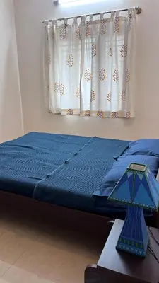 a bed with a blue comforter and a window at Aasana A tranquil space by the hills in Mysore