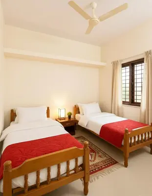 two beds in a white room with a red blanket at Sai Sadan Residency in Lakkidi