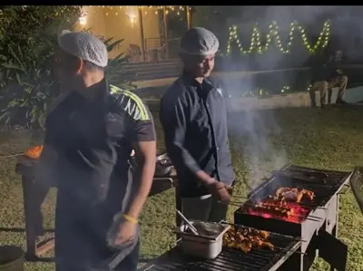 two people standing next to a grill with meat at Tiger Woods Homestay Kabini in Antarasante