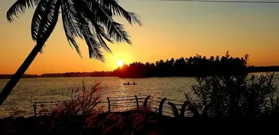 a boat in the water at sunset with a palm tree at Kodamukku water front cottage in Trichūr