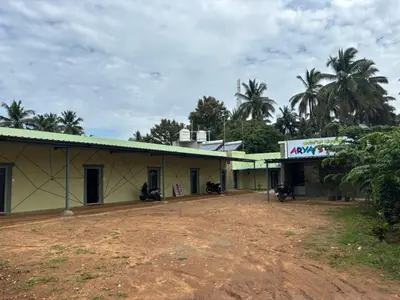 a yellow building with a green roof and palm trees at Aryas comforts Sri Rangapattana in Nāganahalli