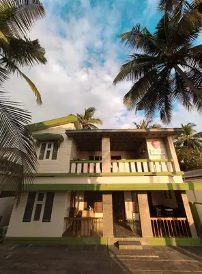 a building with palm trees in front of it at Thekkini rooms and Dorms in Kozhikode