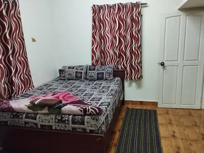 a small bedroom with a bed with a red and white curtain at Arnold Home Stay Ooty in Ooty