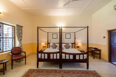 a bedroom with two canopy beds and a chair at amã Stays & Trails - Woshully Bungalow, Coorg in Gonikoppal