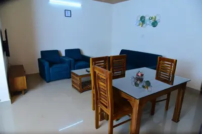 a living room with a table and chairs and a couch at Nirantara Luxury Service Apartment in Gonikoppal