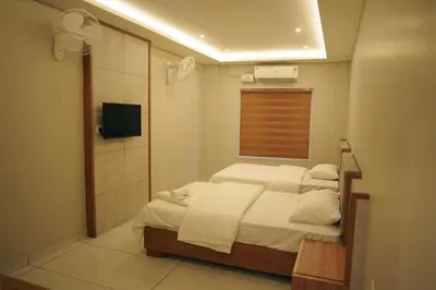 a bedroom with a bed with white sheets and a television at Neom Inn in Wayanad