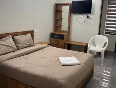 a bedroom with a bed with a chair and a television at Hotel Alka Inn Residency Wayanad in Sultan Bathery