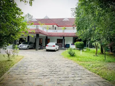 a house with two cars parked in a driveway at Lush Orchard in Kizhake Chālakudi
