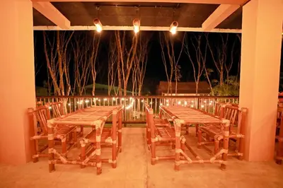 two wooden tables and chairs on a porch at night at Bali bamboo in Padinjarathara