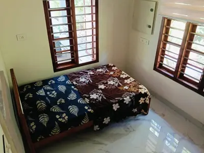 a bedroom with a bed with a floweredspread and two windows at Premium house near Cochin Airport for NRI families in Nedumbassery
