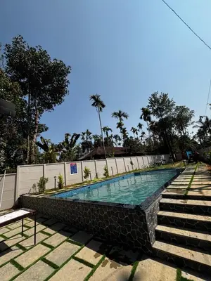 a swimming pool with a stone wall and stairs at Nellarachal Homestay in Ambalavayal