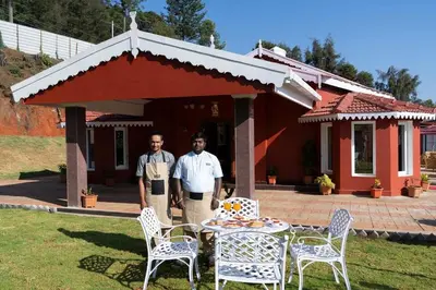 two men standing in front of a house with a table and chairs at Wyncroft Bed and Breakfast, Heritage Bungalow at Kotagiri in Kotagiri