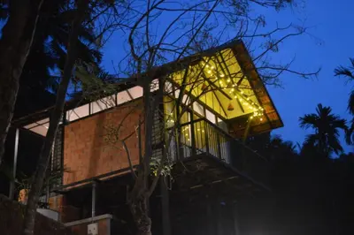 a tree house with a deck at night at Waterfall View Stay Chappanthotam Kozhikode in Kuttyādi