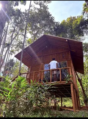 a man standing on the balcony of a tree house at carpa lupa 1 waterfront bamboo cottage wayanad in Meenangadi