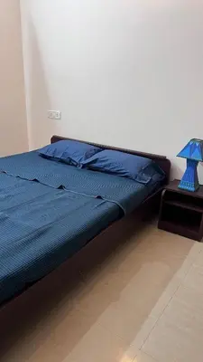 a bed with a blue comforter and a table with a lamp at Aasana A tranquil space by the hills in Mysore