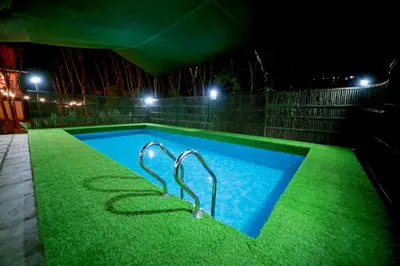 a swimming pool at night with green grass at Bali Bamboo Resort in Padinjarathara