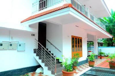 a white house with a staircase and a orange door at Grace Guest Home in Trichūr