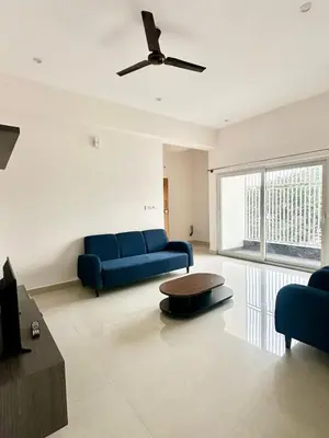 a living room with a blue couch and a ceiling fan at Dakshima Residency in Mysore