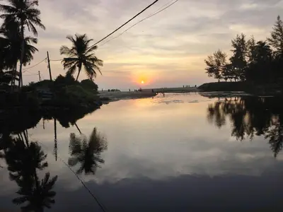 a sunset over a body of water with palm trees at Pratheeksha Homestay in Kannur
