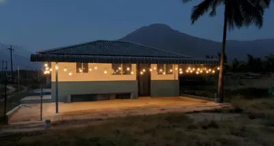 a building with lights on it with a palm tree at Thulir Farm Stay Near Isha Yoga Adiyogi in Coimbatore