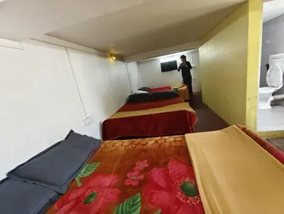 a room with three beds and a person standing in a room at KINGS Home Stay in Ooty