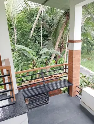 a swing on the porch of a house with palm trees at Izzath Villa in Kottakkal