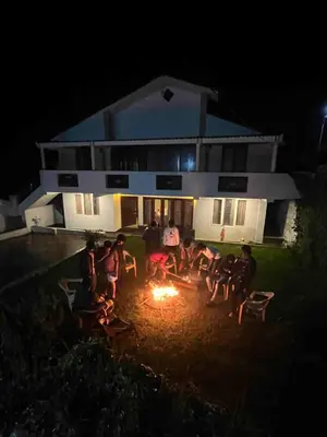 a group of people sitting around a fire in front of a house at Hill Side Cottage in Ooty