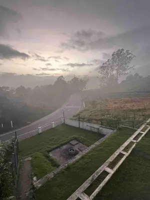 a road in the middle of a field next to a road at Hill Side Cottage in Ooty