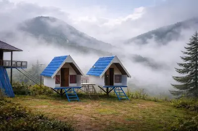 two tiny houses with blue roofs in the mist at Moonhills Cabins in Vattavada