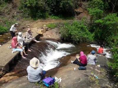 a group of people sitting on a rock by a stream at Oak and Sky Adventures, Kanthalloor in Kanthalloor